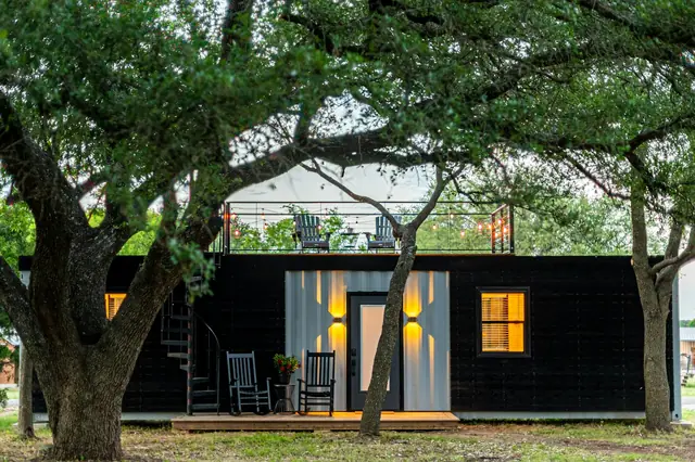 A small backyard cottage under an oak tree, its windows lit