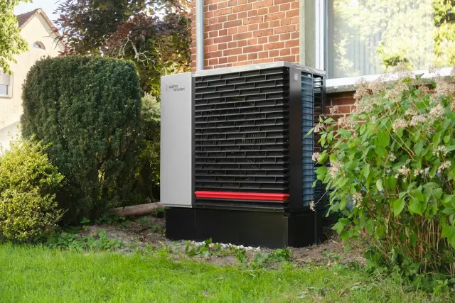 An outdoor heat pump unit on the lawn beside a brick house